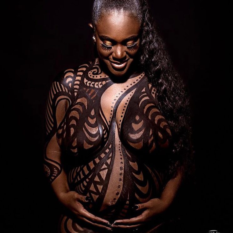 Photo of woman with black swirls body paint and cradling her pregnant belly.