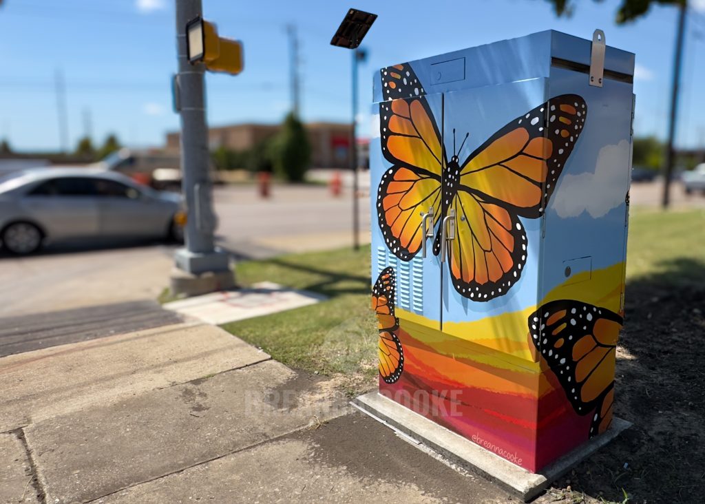 Traffic box with a vinyl wrap of monarch butterflies with street and cars in background.